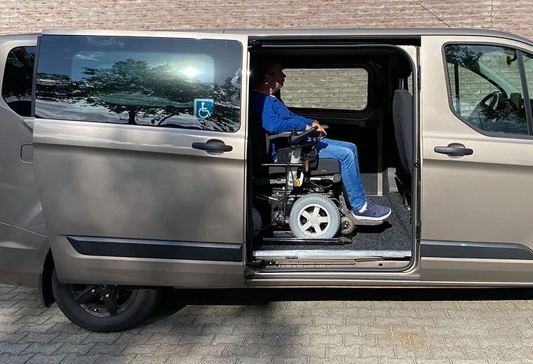 Rollstuhlfahrer im Elektrorollstuhl auf der Liftplattform in der Schiebetür eines Busses