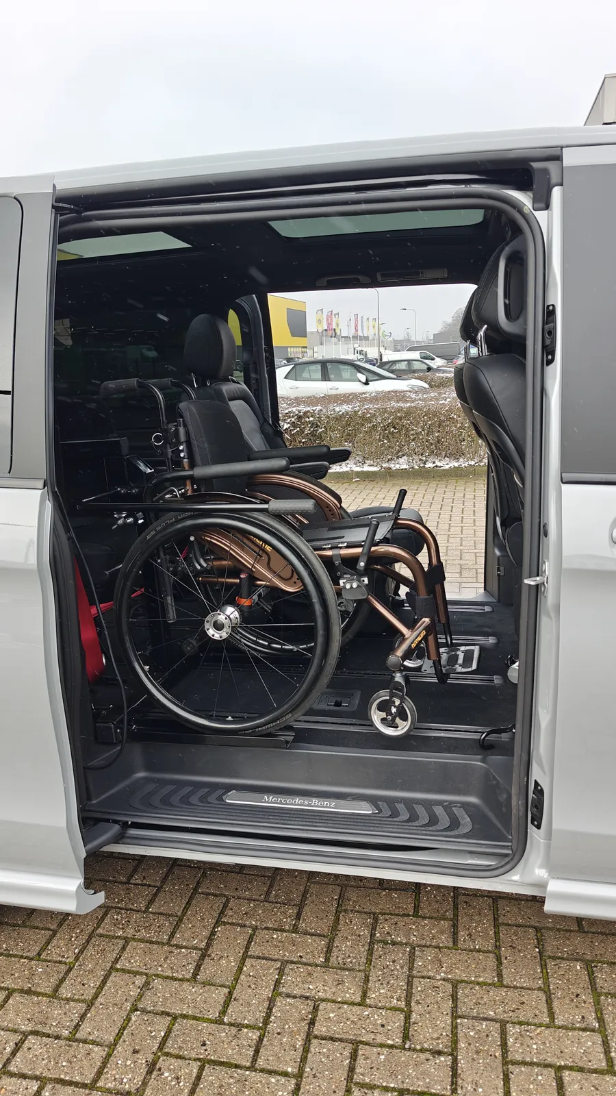 Rollstuhl auf dem Rolpollo-Lift hinter der Schiebetür, in der zweiten Sitzreihe des Personenbusses